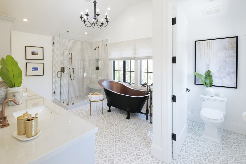 A Spanish-inspired main bathroom with patterned floor tiles, matte black claw foot tub and walk-in shower