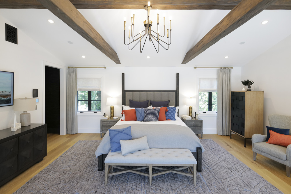 A large main bedroom with a pitched ceiling, chunky crossbeams and bold pops of colour with the decor pieces