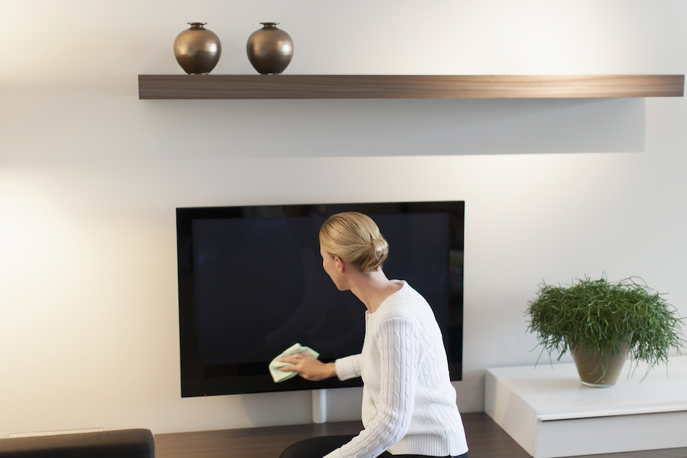 woman dusting television in white living room