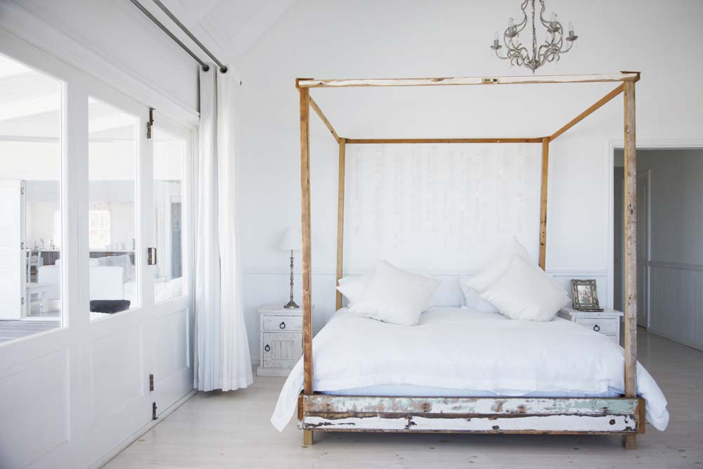 A homemade wooden canopy bed frame in an otherwise pristine white monochromatic bedroom