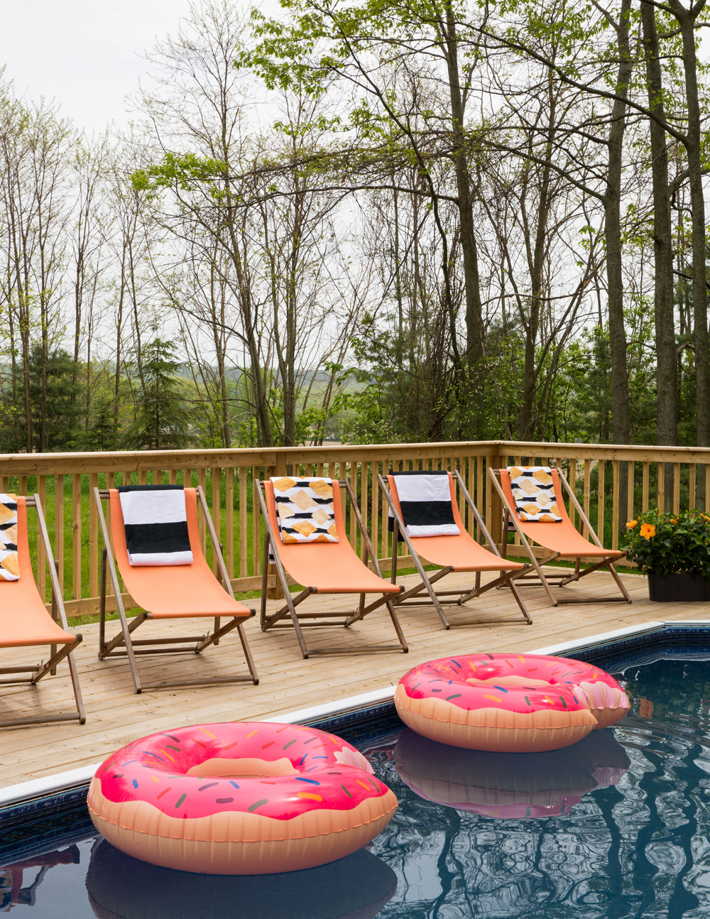 Coral sling chairs poolside with donut-shaped floating devices in the water