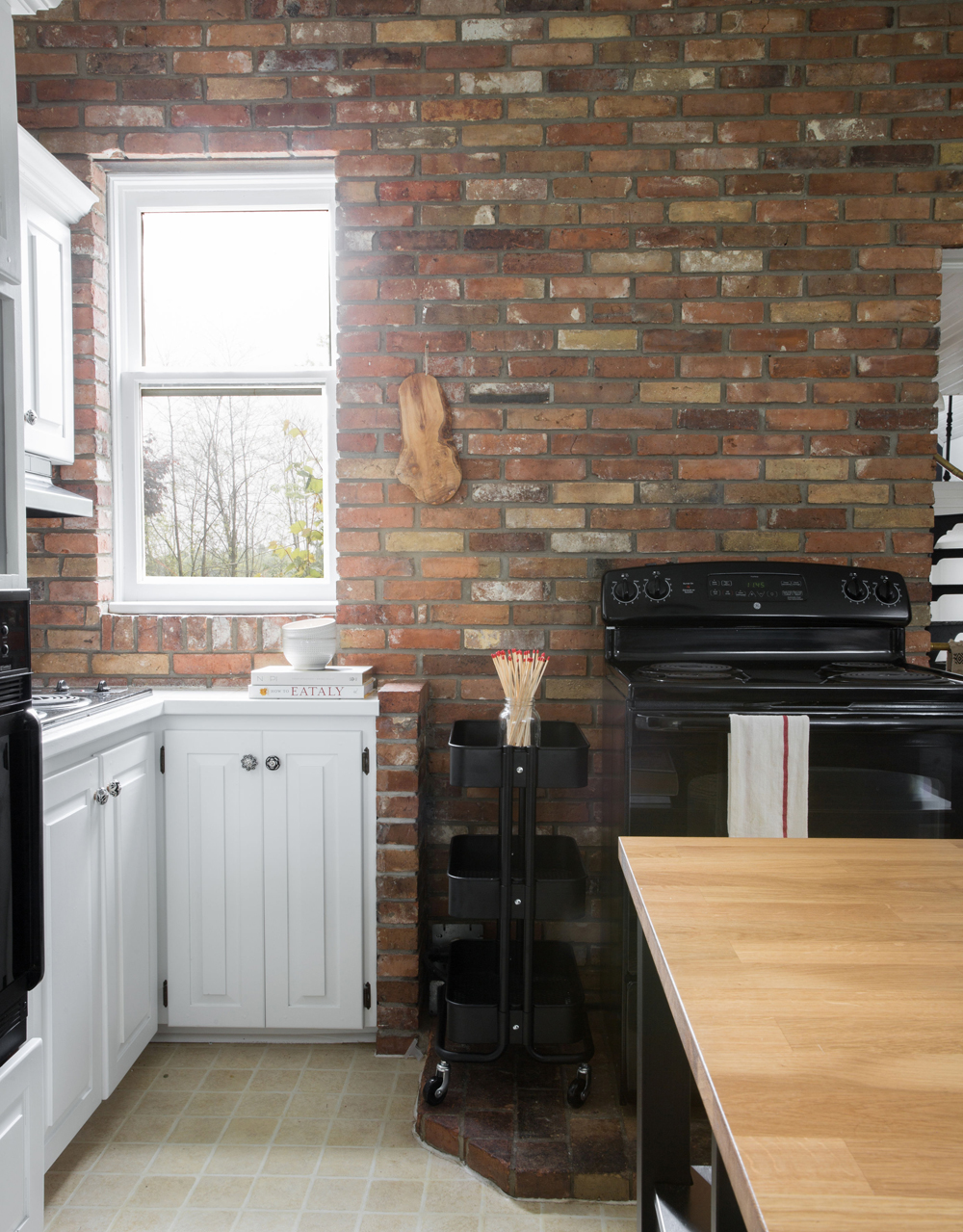 The exposed brick wall in the all-white kitchen lends the space a country-home vibe