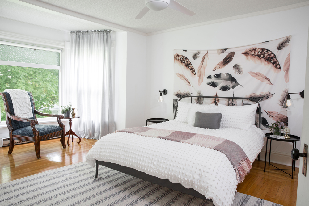 A renovated bedroom with a neutral colour palette and whimsical feather artwork over the bed