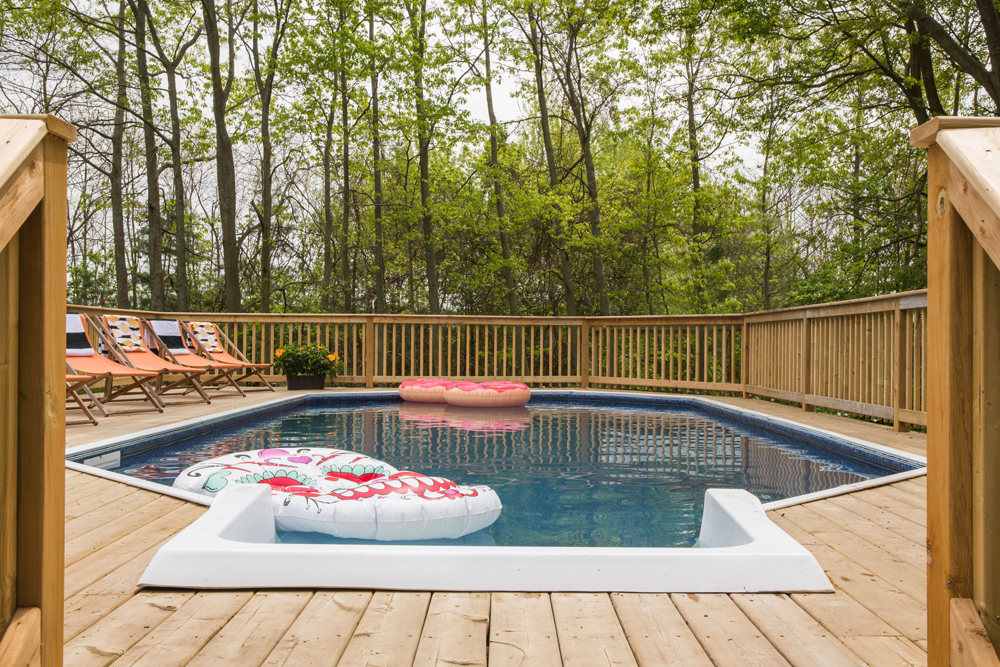 An on-ground pool that is partially in-ground and above-ground surrounded by wood patio