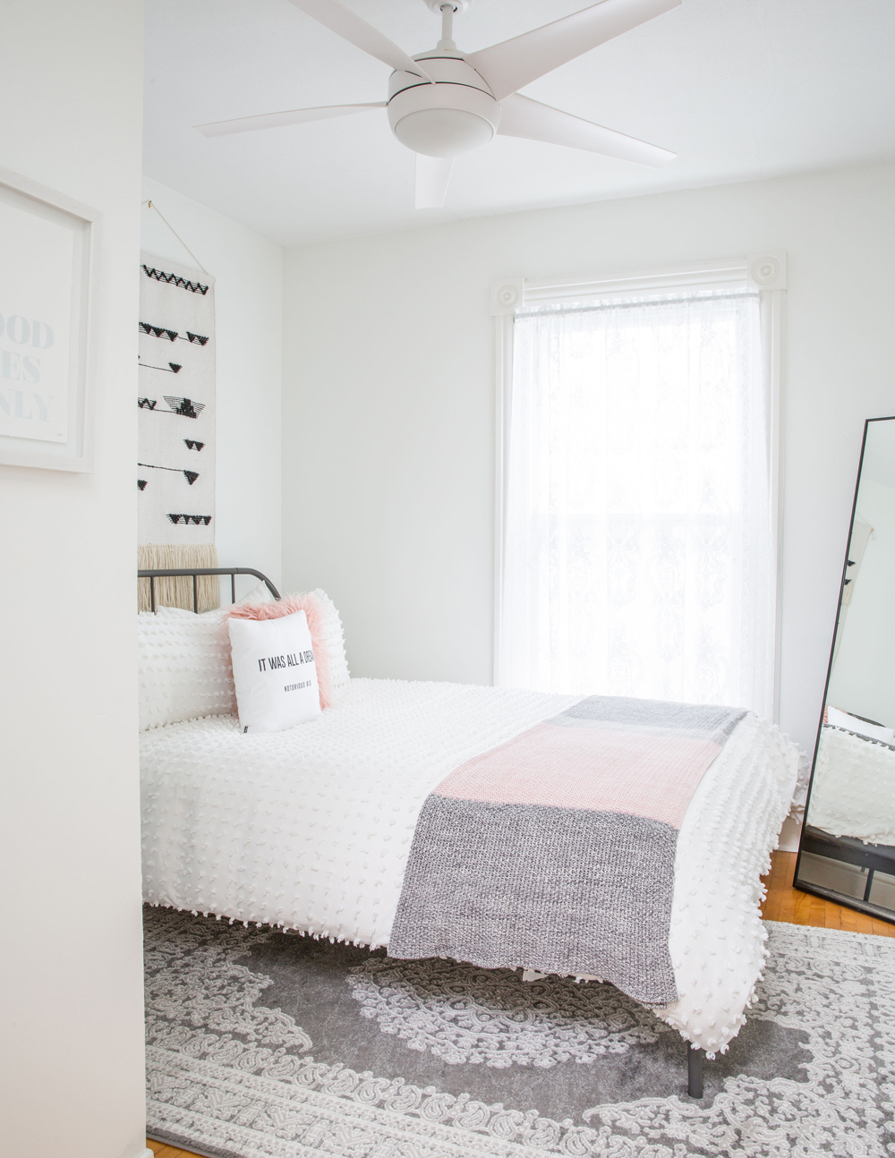 Small white bedroom with grey area rug and macrame wall art
