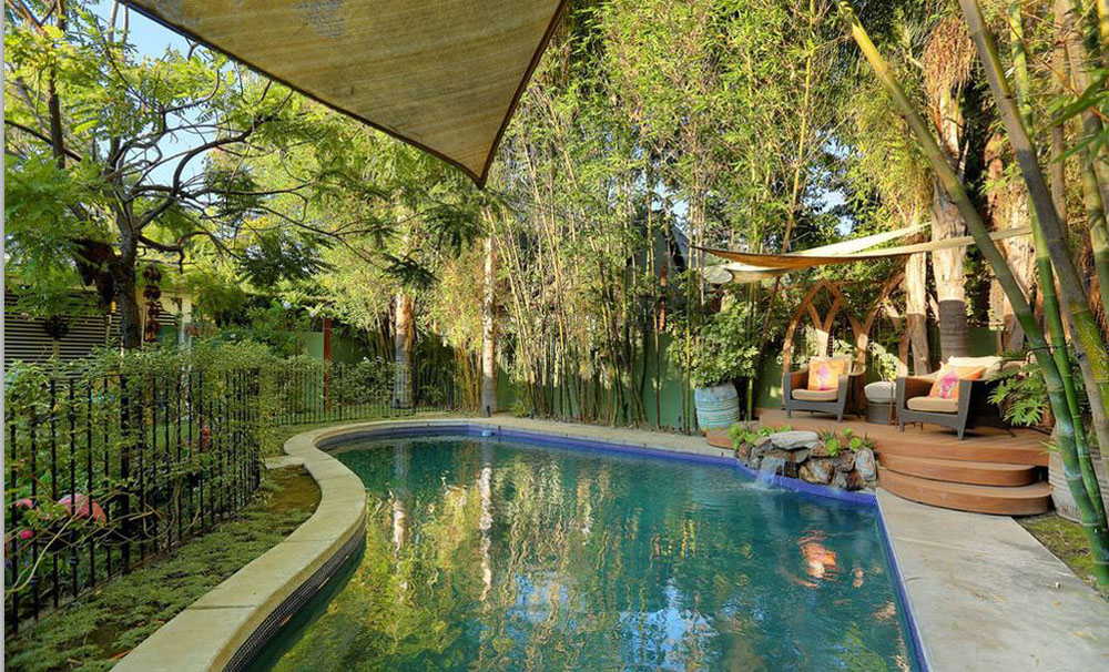 A small outdoor pool shaded by trees and surrounded by patio chairs