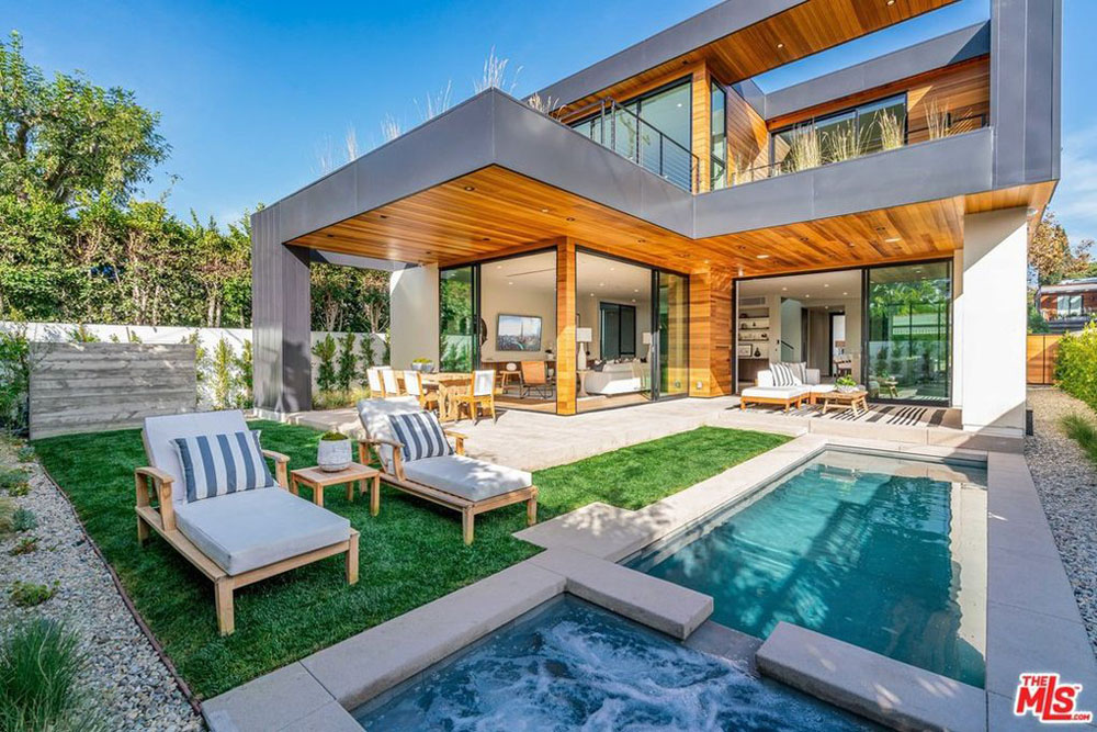 A four-bedroom, four-bathroom 3,500 square feet mostly glass house seen from the backyard where it features a lap pool and lawn furniture