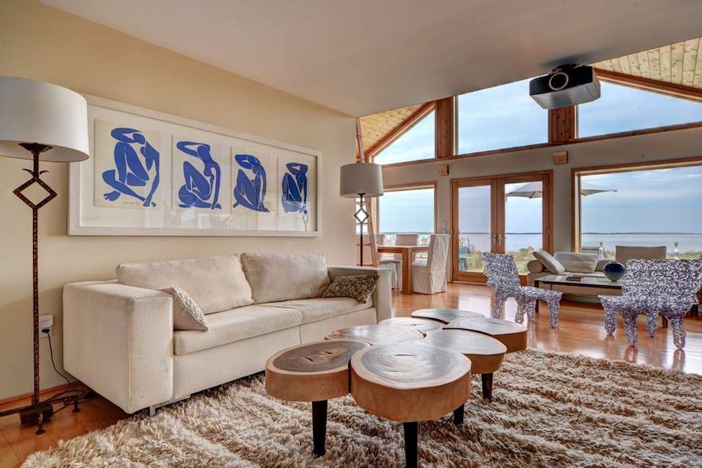 A neutral cottage-inspired living room with a shag throw rug next to windows facing the waterfront