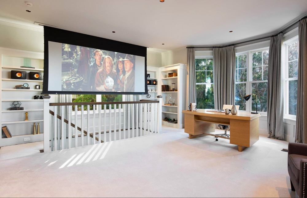 An upstairs home office with a pull-down movie screen and beautiful bay windows overlooking the property