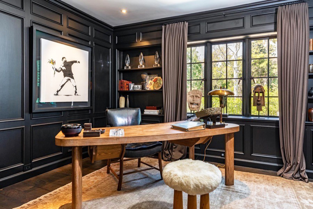 A black panelled home office with oblong wood desk. leather chair and various knick knacks and pieces of art