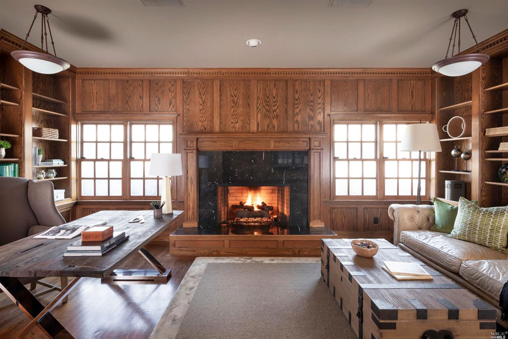 A wood-panelled home office with wood-burning fireplace, wood rectangular desk and couch