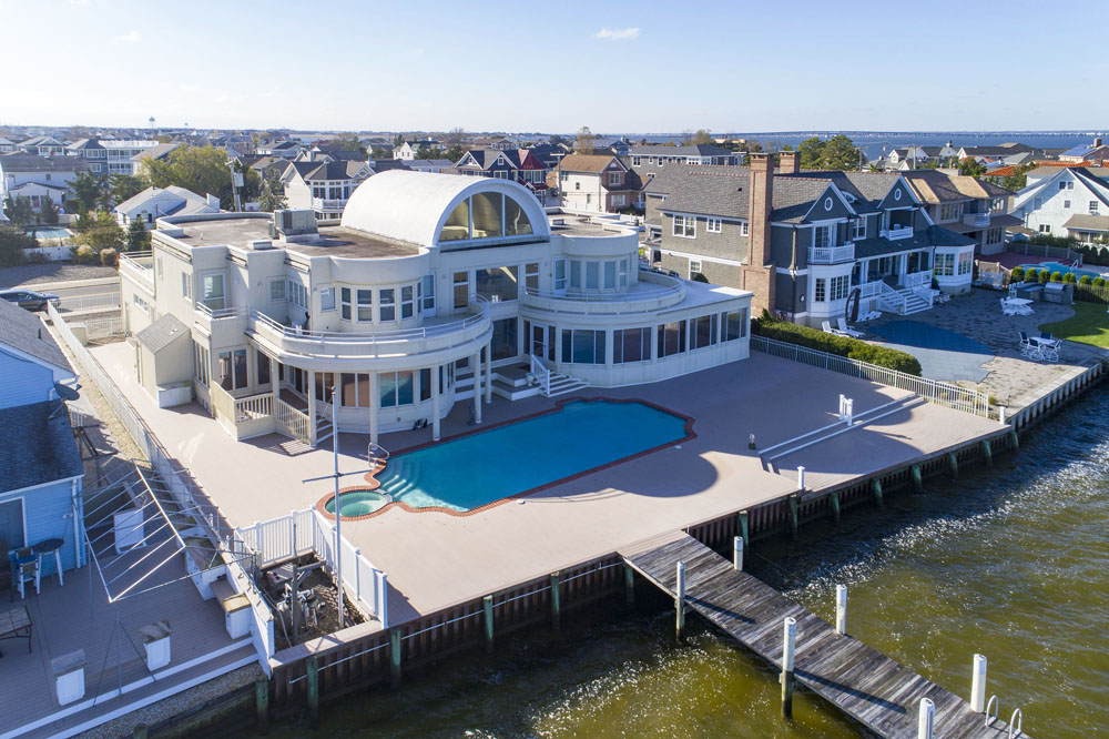 An aerial shot of a waterfront Jersey Shore mansion with a backyard swimming pool and private dock leading out onto the water