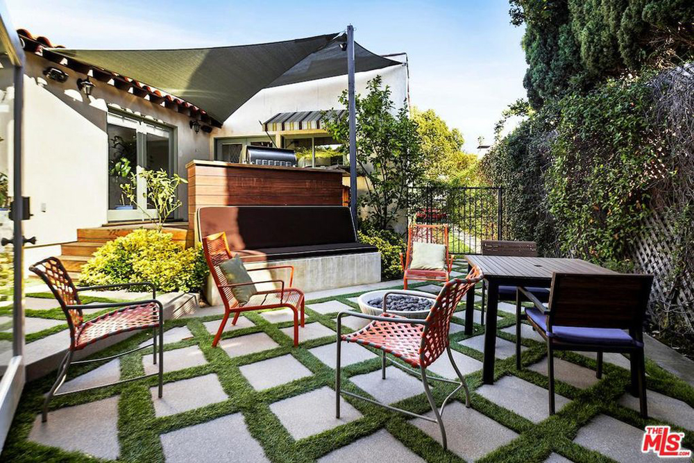An outdoor dining area with a criss-cross brick-and-grass patio with a high trellis with thick climbing vines for privacy