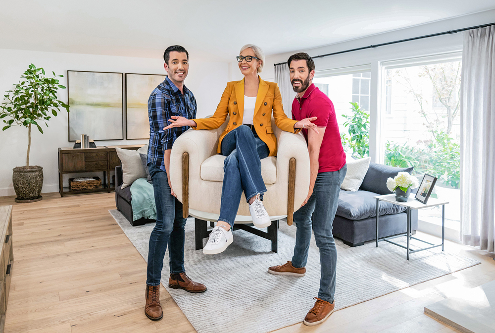 Jonathan and Drew Scott lift up Allison Janney who is sitting in a chair in the renovated living room