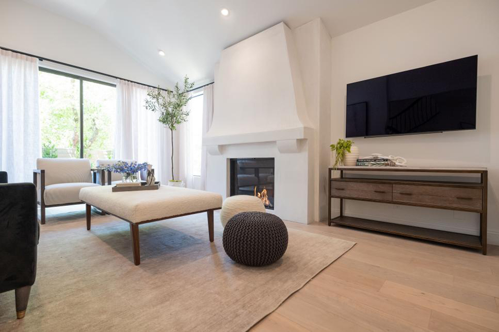 A renovated living room with wide-plank oak hardwood floors, shutter-less windows and floor-to-ceiling fireplace