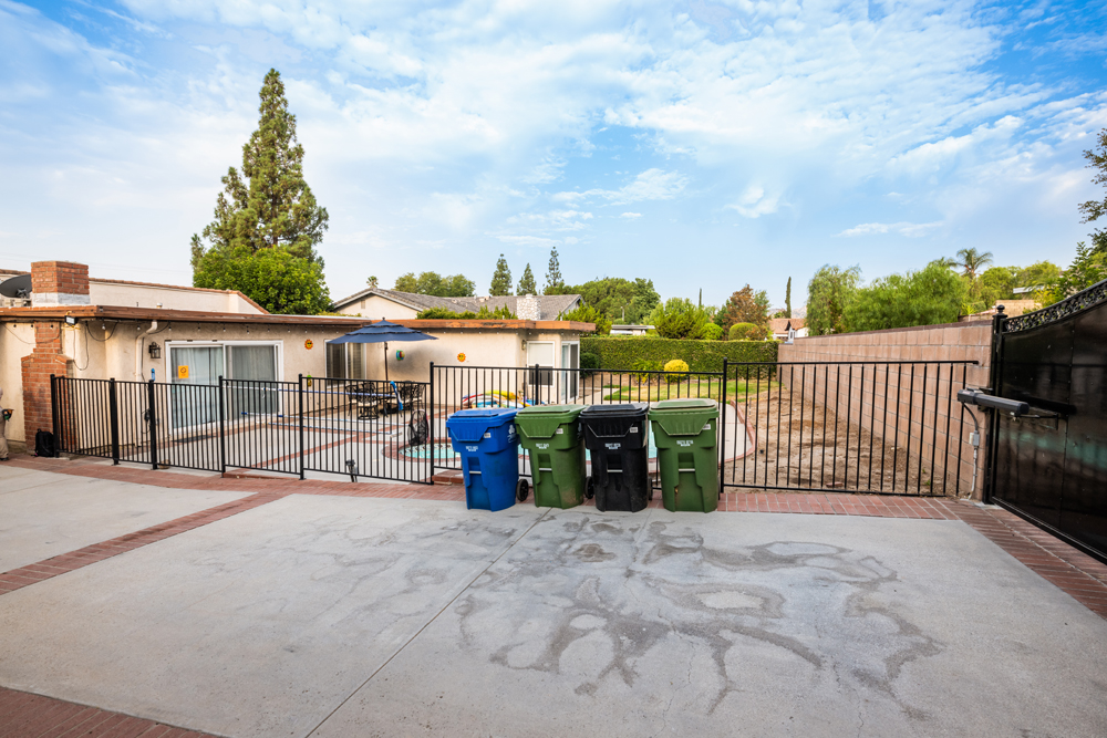 An outdated, rundown backyard with an empty pool and garbage bins lined up outside the gate