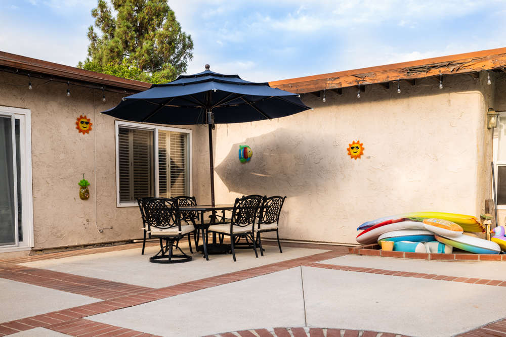 A simple four-seater table shielded by an umbrella and off to the side of the pool by the back door exit