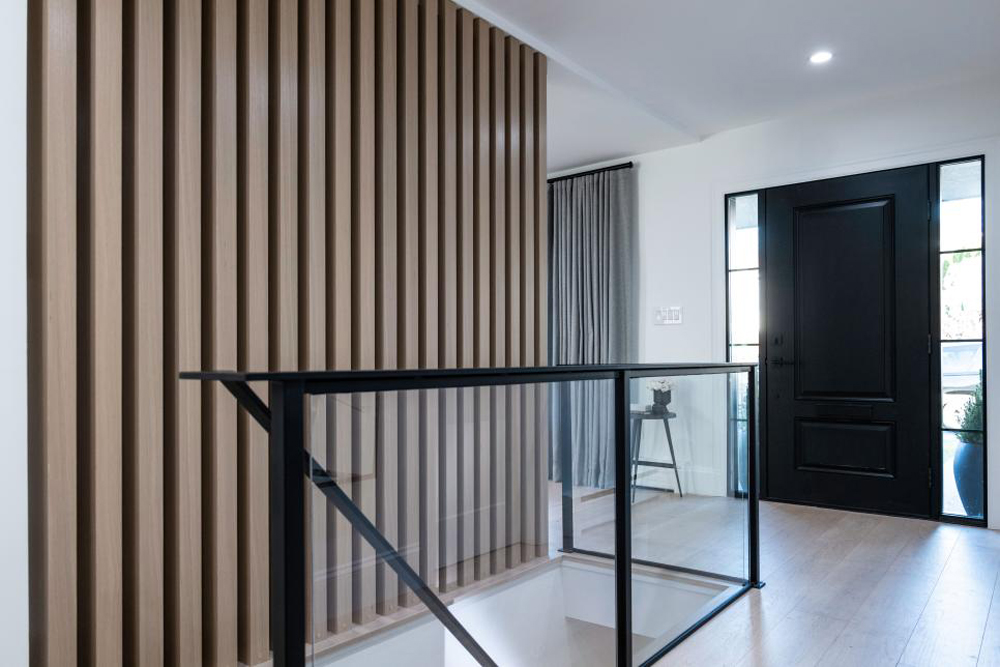 A gorgeous oak slat wall and glass staircase in the renovated entryway