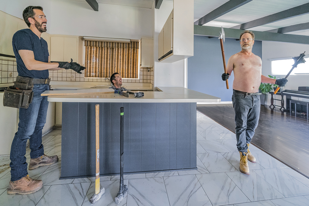 A topless Rainn Wilson holds medieval weaponry as the Property Brothers laugh while renovating the kitchen
