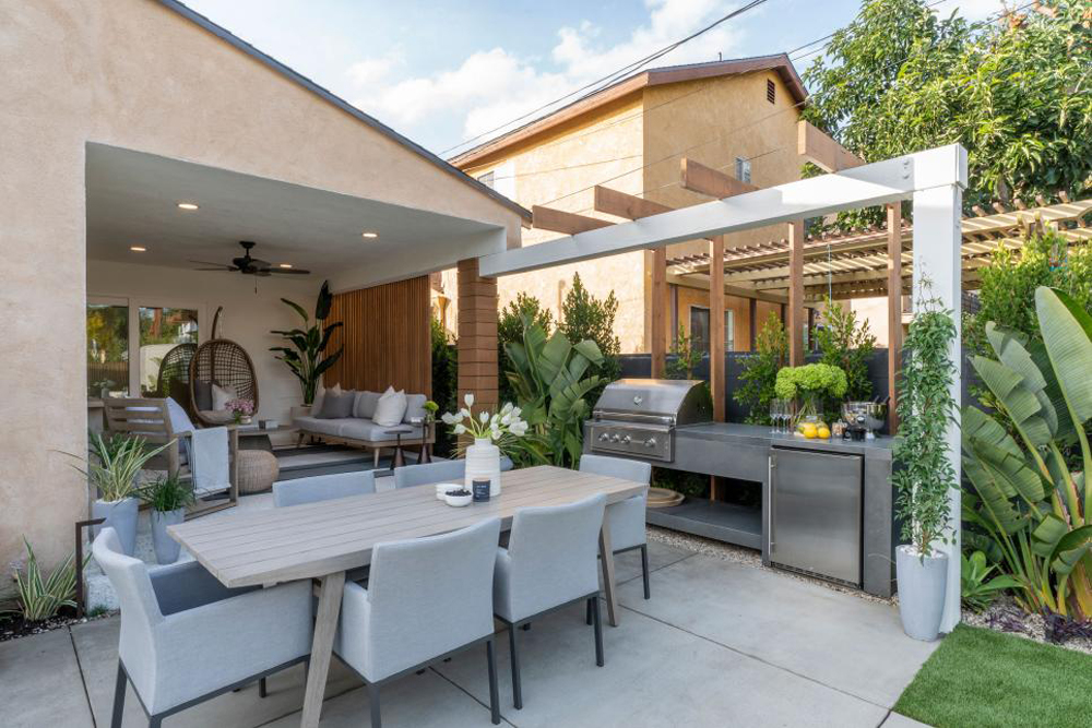 The renovated backyard features an outdoor dining space complete with a stainless steel grill and refrigerator