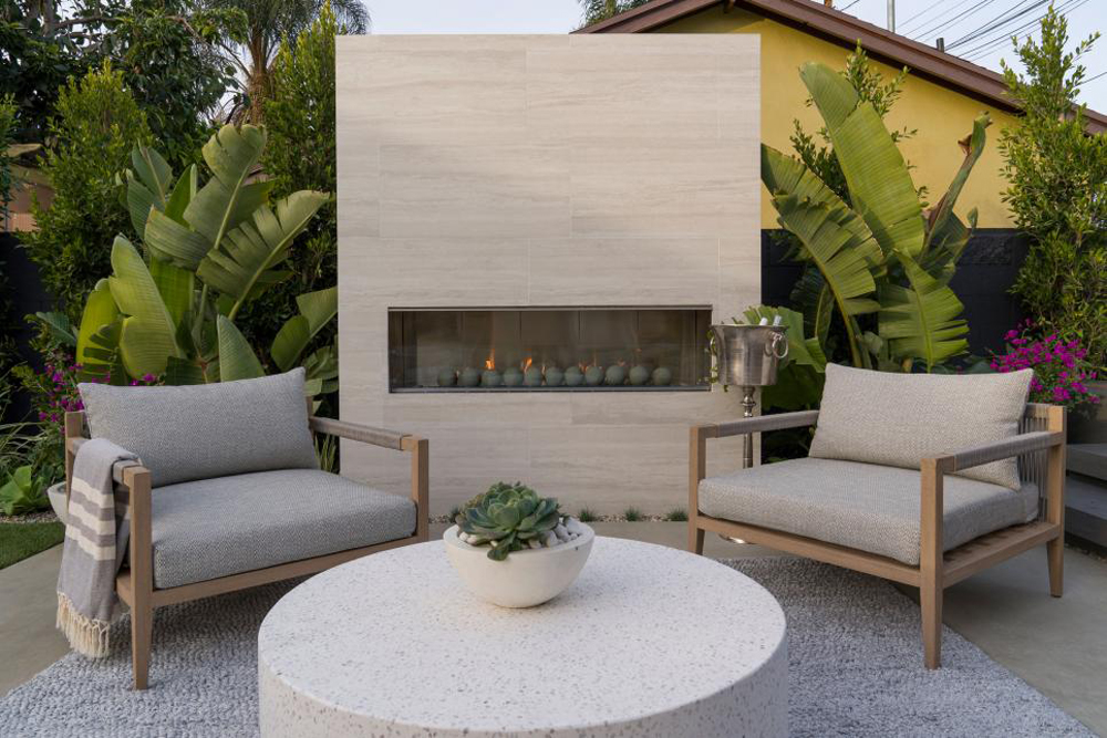 The backyard features a linear fireplace with ceramic balls and neutral furniture