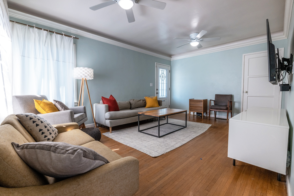 The pre-renovation living room with pastel blue walls, hardwood flooring, minimalist furniture and plenty of natural light