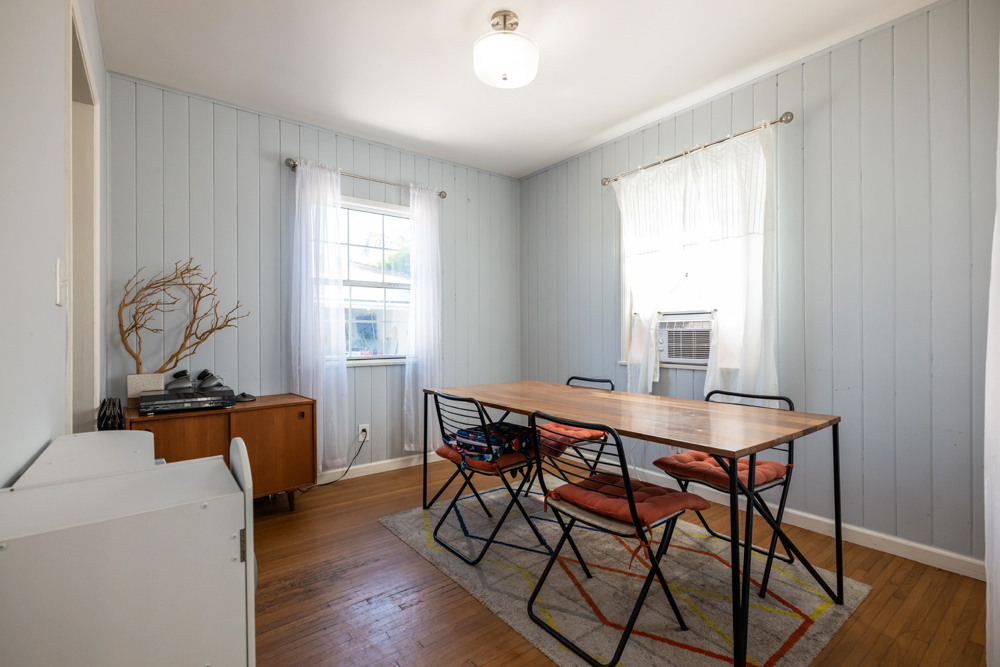 A narrow, outdated dining room with a plain wood table and shiplap walls