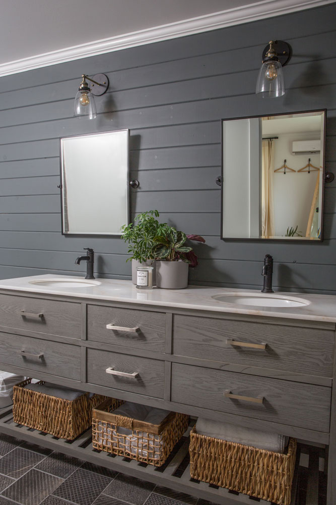 grey bathroom with grey wood vanity, two sinks, three wicker baskets below