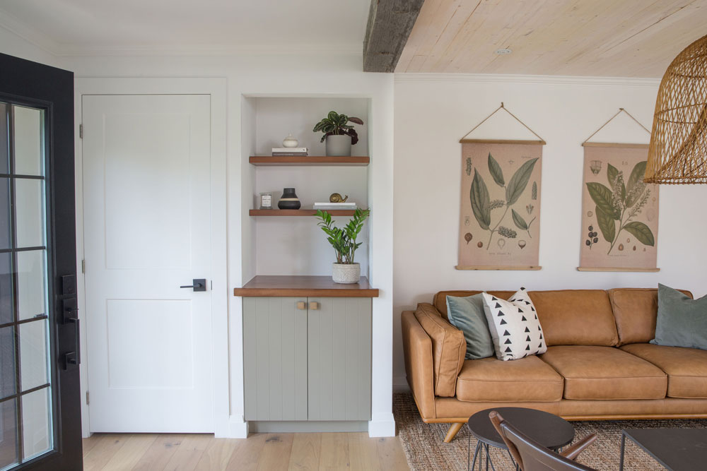 niche beside tan leather sofa with two wood shelves and bottom cupboards painted light mossy green