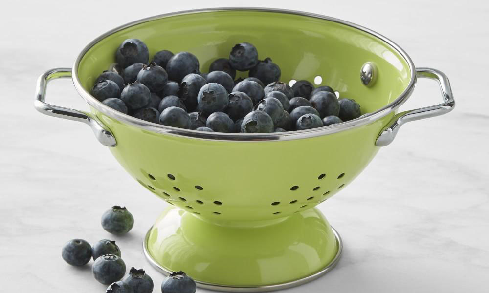 A green enamelled colander filled with blueberries