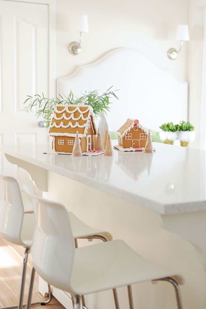 two gingerbread houses in white kitchen with two white bar stools