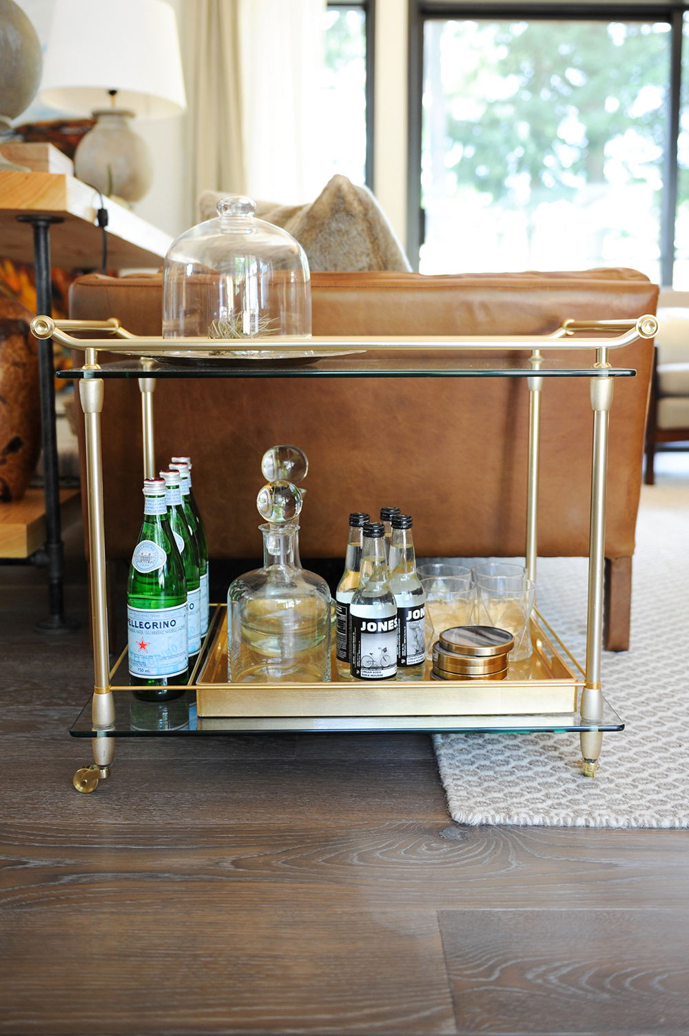 A gold and glass bar cart filled with drinks and glasses