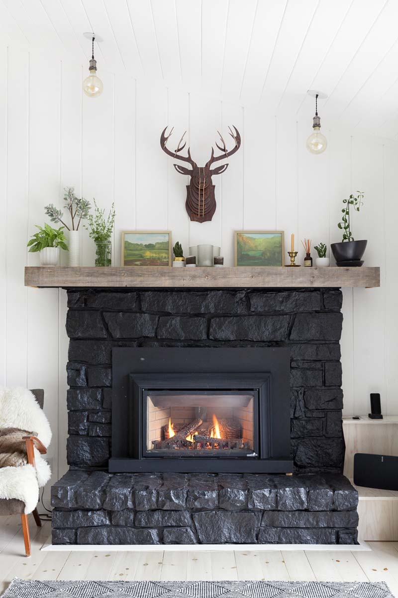 A brick fireplace painted black with faux deer antlers hanging above the mantle