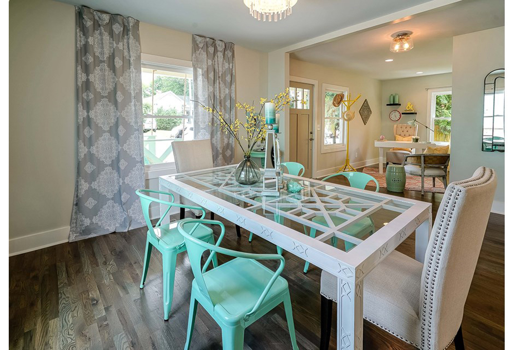 A white glass dining table with aqua chairs in a room featuring billowy patterned curtains