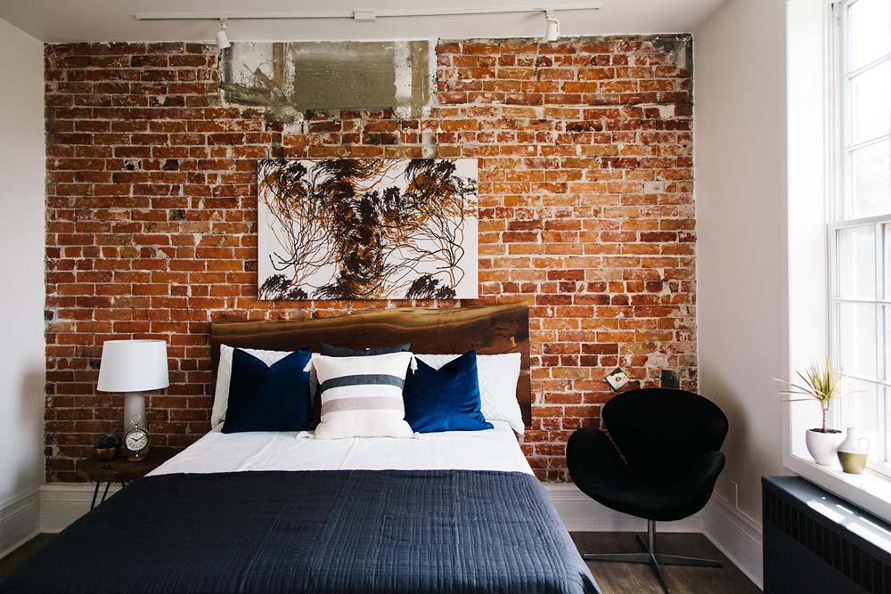 A rustic bedroom with an exposed brick accent wall, deep blue throw pillows and a wooden headboard