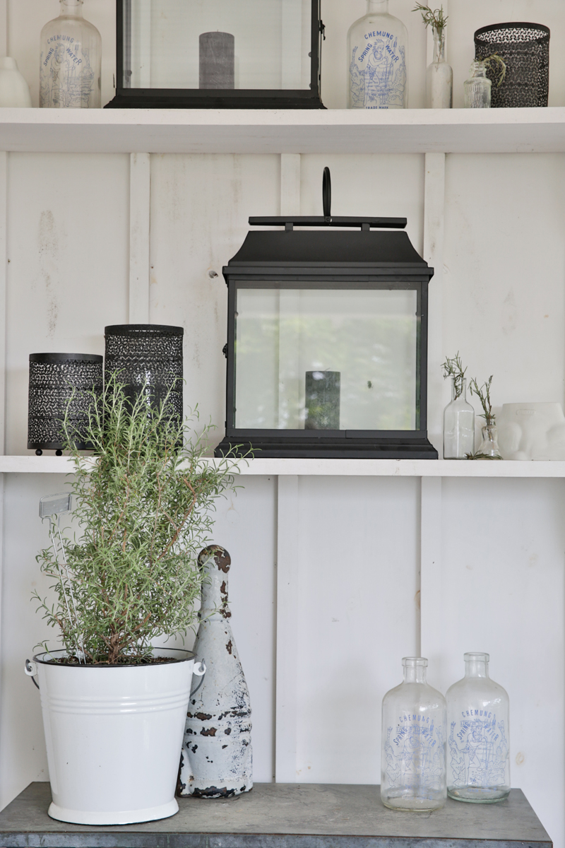White rustic shelving with a variety of plants, bottles and lanterns