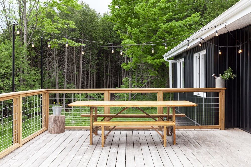 An expansive outdoor patio area with a picnic table overlooking a forest and light strings overhead