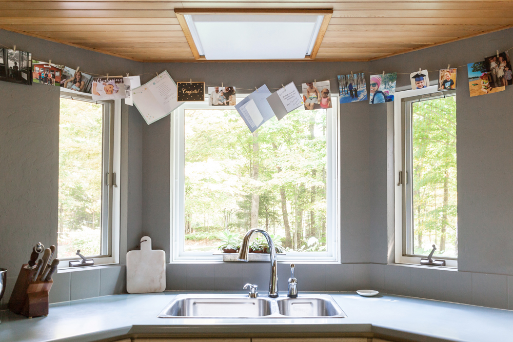 A kitchen sink area with a window overlooking the trees with a string of personal momentos hanging from above