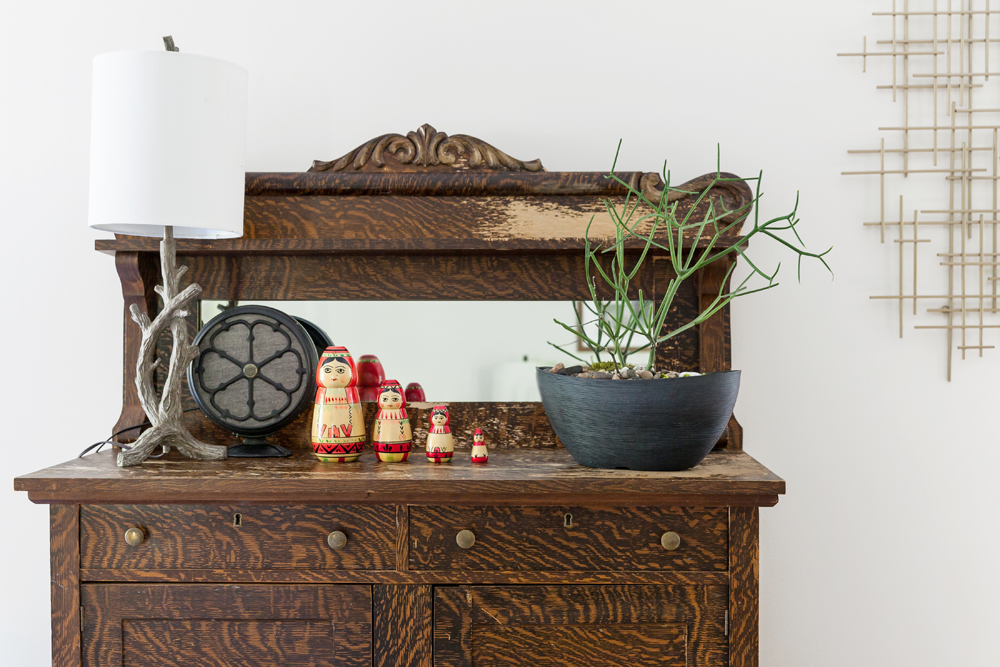 A rustic wooden cabinet with various knick knacks, including a branch lamp, potted plants and Russian nesting dolls