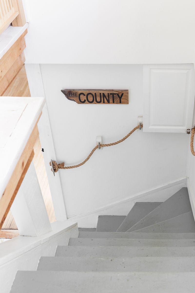 A carpeted spiral staircase with rope handrails and a rustic wood sign hanging on the wall