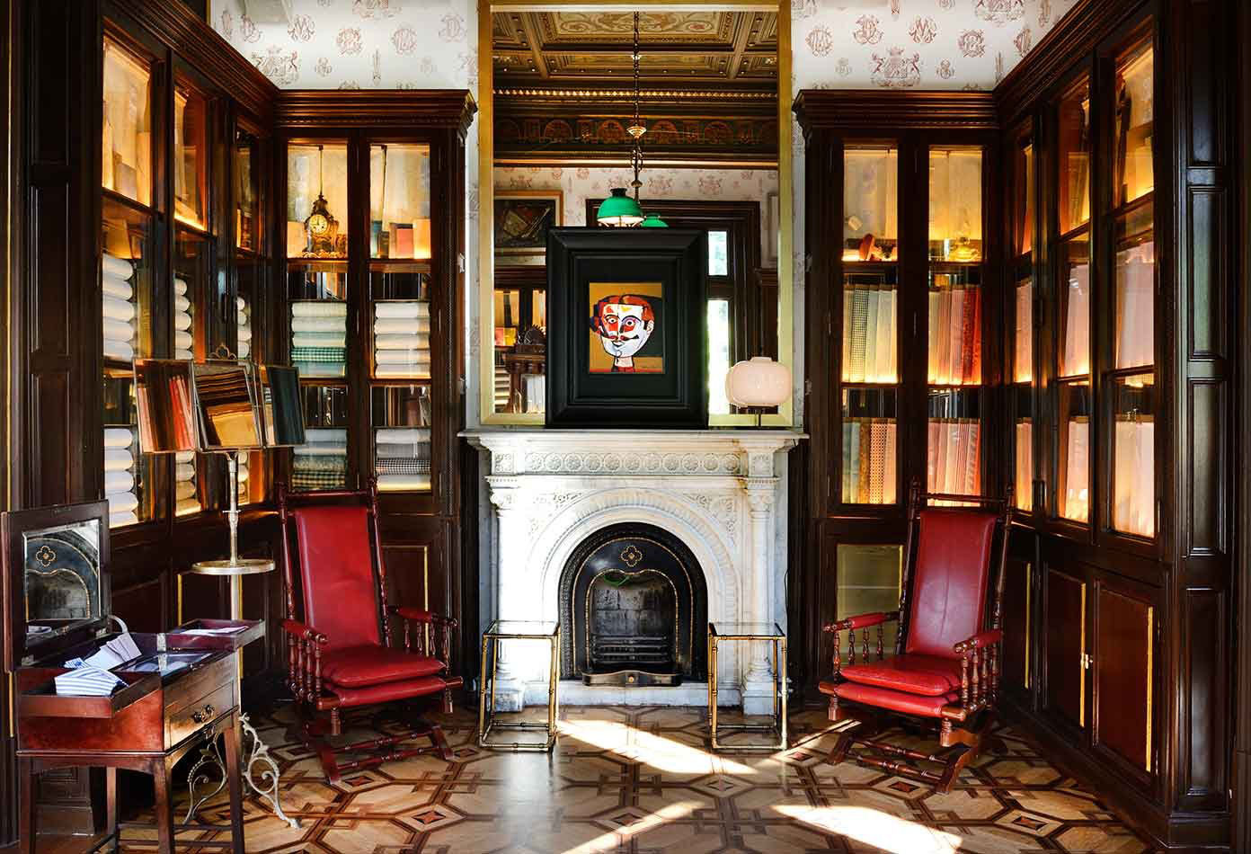 glass front bookcase lined room with marble fireplace, two red leather chairs, picasso-like pic on mantel