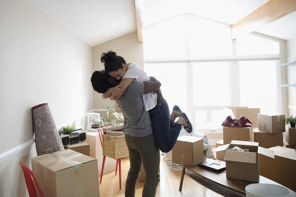 A young couple embrace in their home surrounded by packing boxes