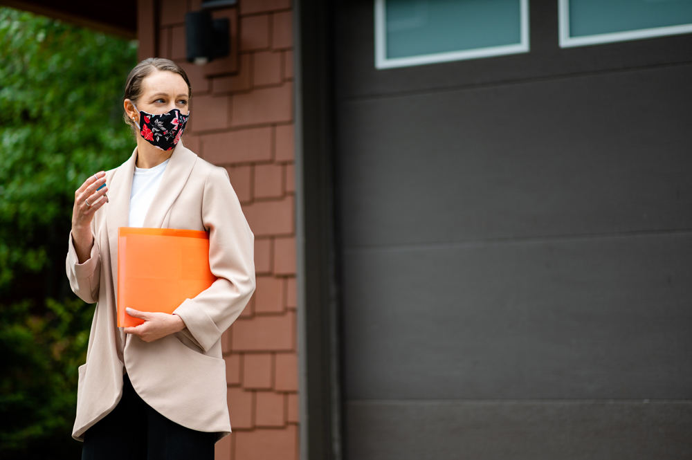 A woman leaving a house, carrying a folder and wearing a cloth face mask