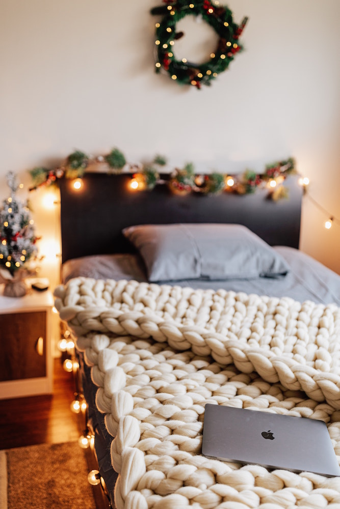 winter bedroom with cream-colour chunky knit blanket on bed and holiday decorations on wall