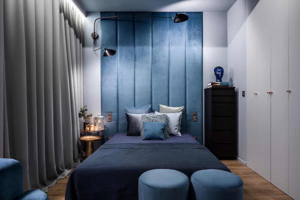 monochromatic blue bedroom with dark blue bed and dark upholstered wall behind the bed