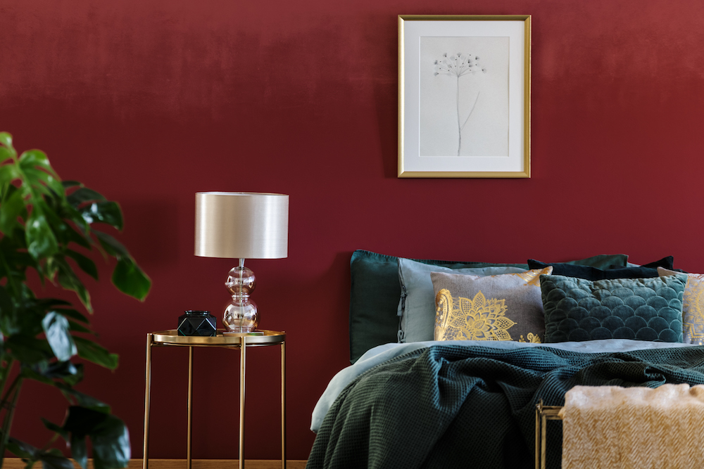 lamp on table next to bed with green bedding in sophisticated red bedroom interior with poster