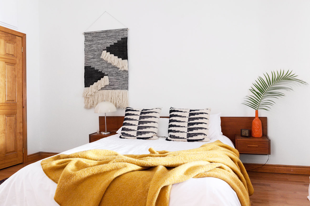 A minimalist bedroom with macrame wall art, potted plants and low-to-the-ground bed and nightstands