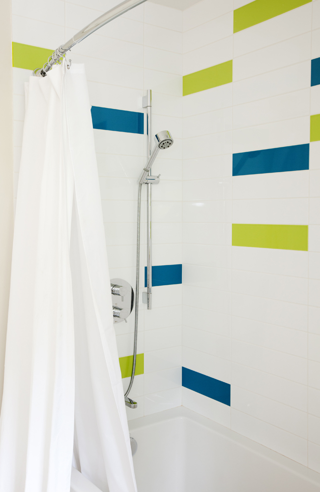 A shower featuring colourful blue and green tiles.