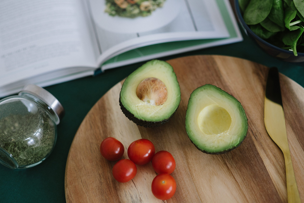 An avocado sliced in two on a cutting board with other various ingredients