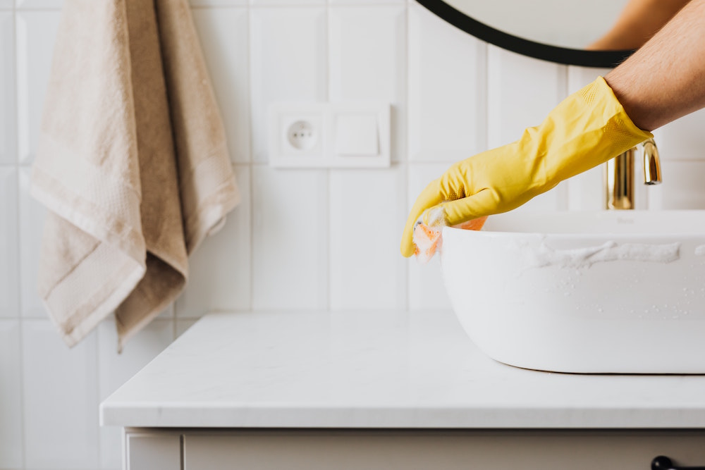 yellow-gloved hand cleaning white bathroom